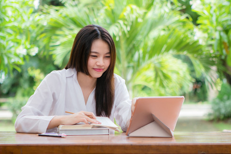 Happy asian woman working on wooden table with blurry tree backgroundの写真素材