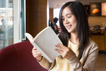 Asian woman reading book inside coffee shop