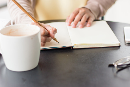 People hand writing with pencil on notebook near by coffee mug and glassesの写真素材