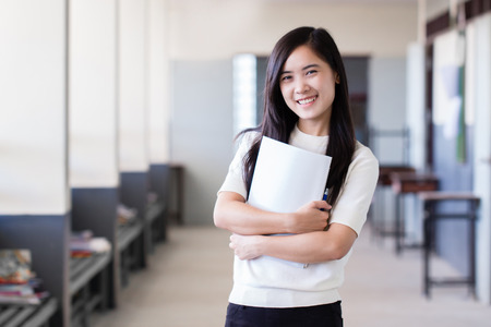 Happy asian woman holding books stand inside school hall wayの写真素材