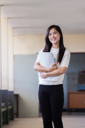 Asian woman holding book inside school hall way with blurry backgroundの写真素材