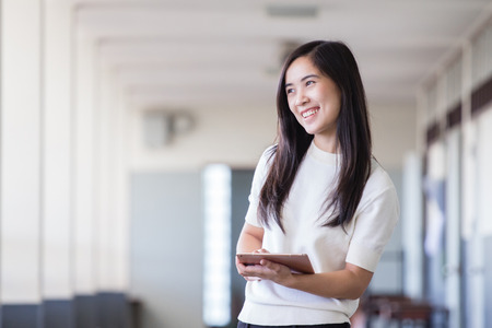 Asian woman using tablet while standing inside university hall wayの写真素材