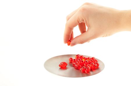 red transparent vitamin pills on a steel round plate. hand with one pill. white backgroundの写真素材