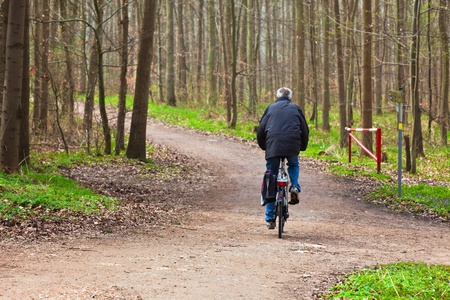 An elderly man riding a bicycle through the woodsの写真素材