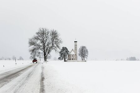 Alpine bavarian Church road and tractor after morning snowfall in mountain villageの写真素材