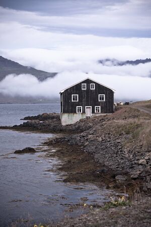 Lonely Black Wooden House at coastline in East Iceland. Vertical toned shot