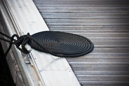 A mooring rope with a knotted end tied around a cleat on a wooden pierの写真素材
