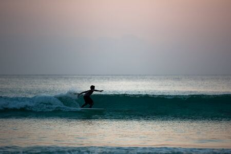 Silhouette of boy surfing on board in ocean shore during sunsetの写真素材