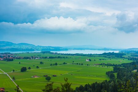 View from Bavarian Neuschwanstein Castle in a summer foggy weather to a field and a lakeの写真素材