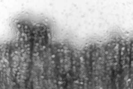 Rain water drops on a window glass surface. Defocused bw blur image with bokeh