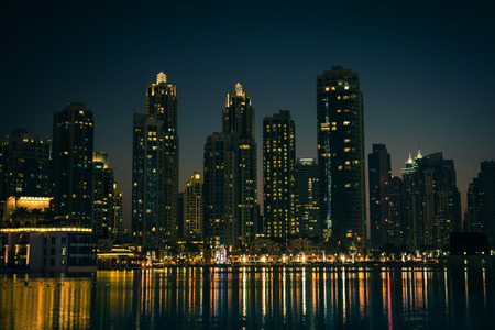 Night cityscape of Dubai city, United Arab Emirates. Reflections in the water. Filtered shot