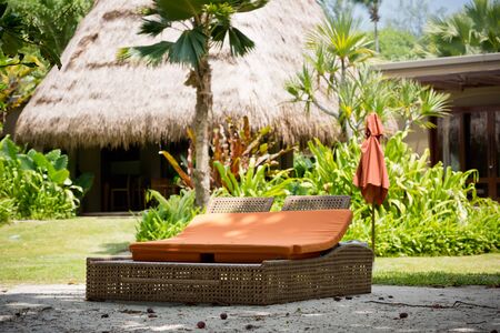 beach bed on white sand among palm trees in full sun