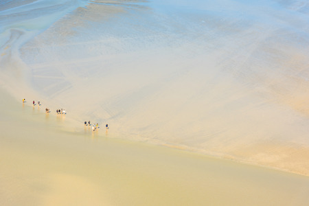 View from walls of Mont Saint Michel on the bay during the low tide with groups of tourists walking. Franceの写真素材