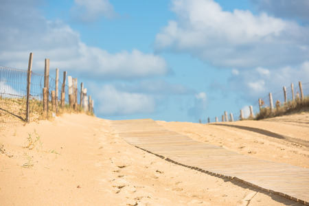 Wooden footpath through dunes at the ocean beach in Western France. Selective focus