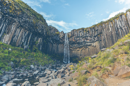 Svartifoss Waterfall in Iceland under a blue summer sky with clouds