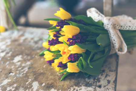 Yellow tulips and purple hyacinths flowers bouquet on a wooden table. Indoors natural light shot with small depth of fieldの写真素材