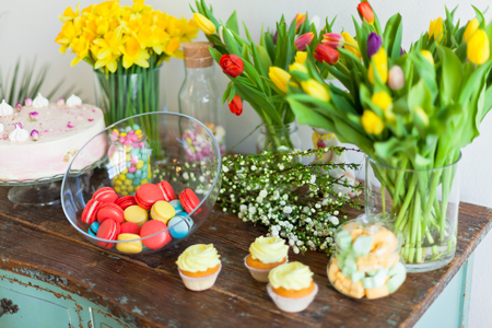 Bright macaroons and cupcakes on a wooden table. Indoors natural light shot with small depth of...