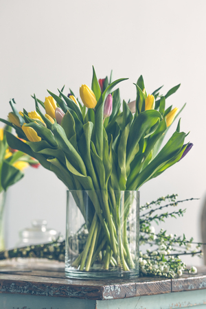 Multicolored tulips flowers bouquet in a glass vase on a wooden table. Indoors natural light shot with small depth of fieldの写真素材