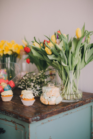 Spring flowers and sweets on an old wooden table. Indoors natural light shot with small depth of...