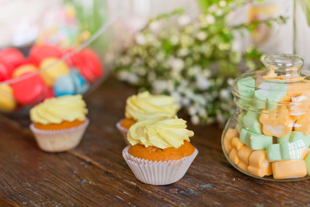 Bright macaroons and cupcakes on a wooden table. Indoors natural light shot with small depth of...