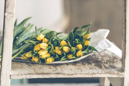 Yellow tulips flowers bouquet on a wooden table. Indoors natural light shot with small depth of fieldの写真素材