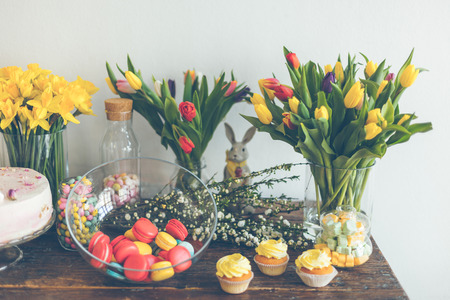 Bright macaroons and cupcakes on a wooden table. Indoors natural light shot with small depth of...