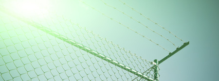 A chain link fence, topped by razor wire. Long wide banner with solar effectの写真素材