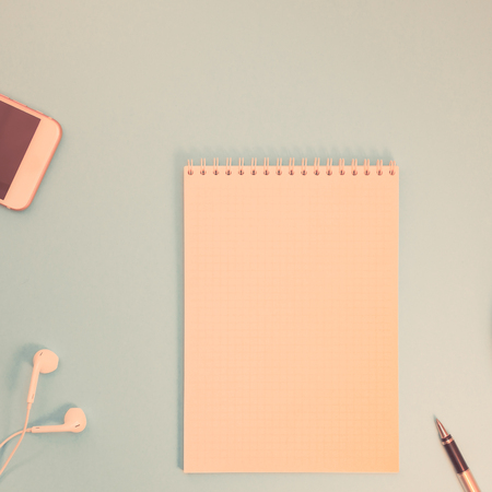 Creative flat lay photo of workspace desk with paper notebook, smartphone, earpieces, pen and coffee with copy space background minimal styleの写真素材