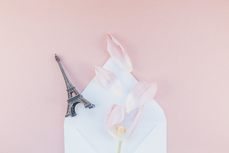 Pink tulip with petals in opened paper envelope letter with eiffel tower miniature on a pink background. Flat lay top view. Romantic love memories conceptの写真素材