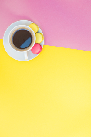 Creative flat lay photo of coffee cup and macaroons with copy space on pink and yellow background minimal styleの写真素材