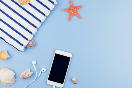 Creative flat lay concept of summer travel vacations. Top view of beach towel, seashells, starfish and smartphone on pastel blue background with copy space in minimal style, template for textの写真素材