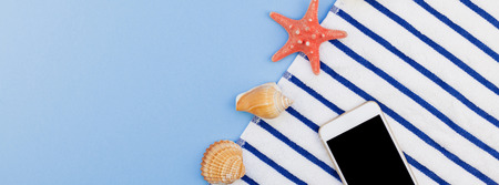 Creative long wide banner flat lay concept of summer travel vacations. Top view of beach towel, seashells, starfish and smartphone on pastel blue background with copy space in minimal style, templateの写真素材