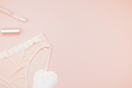 Feminine flat lay set of female panties and accessories, perfumes, lipstick and pads liners on pastel pink color background for fashion blog and social media with copy space for textの写真素材