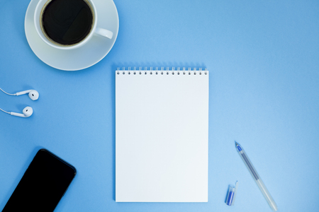 Creative flat lay photo of workspace desk with paper notebook, smartphone, earpieces, pen and coffee with copy space background minimal styleの写真素材