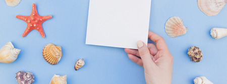 Creative long wide banner flat lay concept of summer travel vacations. Top view of seashells and starfish on pastel blue background with postcard mock up and copy space in minimal style, templateの写真素材