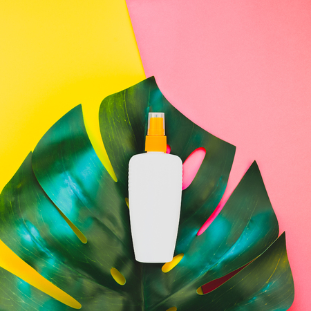 Tropical jungle palm monstera leaves and sunscreen blank bottle mockup on bright square yellow and pink dualtone paper background.の写真素材