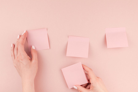 Creative flat lay photo of workspace desk with millennial pink sticker paper post it mock up in woman hands holding and gluing them on wall with copy space background minimal style. Template for textの写真素材
