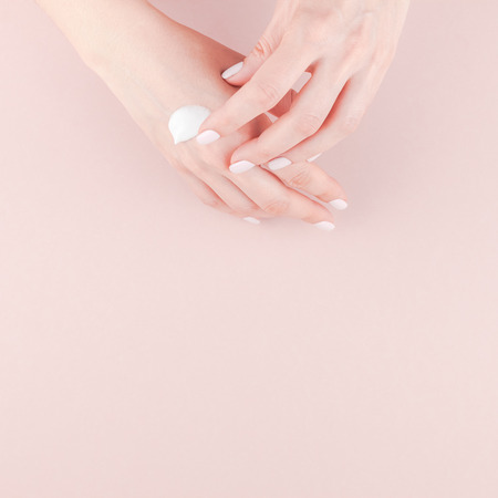 Creative image of woman moisturizing her hand with cosmetic cream lotion with copy space on millennial pink background in minimalism style. Square Concept for feminine blog social media beauty conceptの写真素材