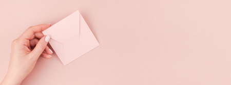 Long wide banner of woman hand holding small love letter with copy space on millennial pink background in minimalism style. Concept template for feminine blog, social mediaの写真素材