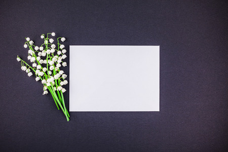 Creative flat lay top view mock up with fresh bouquet of lilies of the valley on a black paper background with blank white letter frame and copy space in minimal style, template for textの写真素材