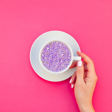 Square flat lay concept top view white cup beautiful lilac flowers floating in infused water and woman hand millennial pink background copy space minimal style template text. Spa wellness conceptの写真素材