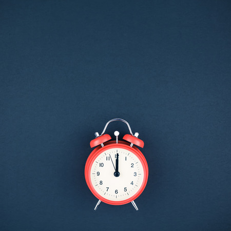 Concept image of a red vintage alarm clock with twelve o clock on dark blue color paper background...