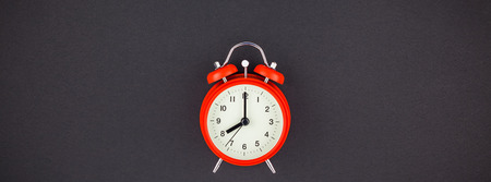 Concept image of a red vintage alarm clock with eight o clock on dark black color paper background...