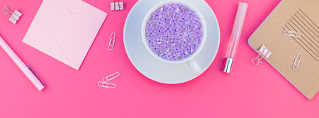 Creative top view flat lay of workspace desk styled design office supplies and cup of tea with copy space on a bright pink color paper long wide banner. Template for feminine blog social mediaの写真素材