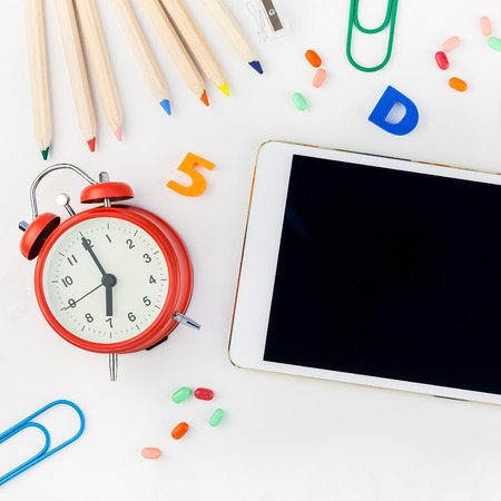 Square flat lay back to school concept blank tablet with alarm clock, color school and office supplies on white table background with copy space, frame, template for text or designの写真素材