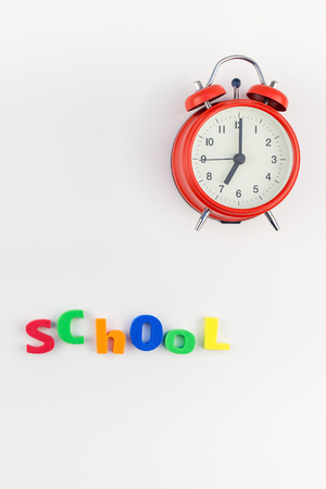 Creative flat lay back to school concept with alarm clock, color school and office supplies on white table background with copy space, frame, template for text or designの写真素材