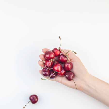 Square top view of fresh ripe cherry in a female hands with copy space isolated on white background in minimal style. Concept of summer fun and healthy eating. Template for your text or food designの写真素材