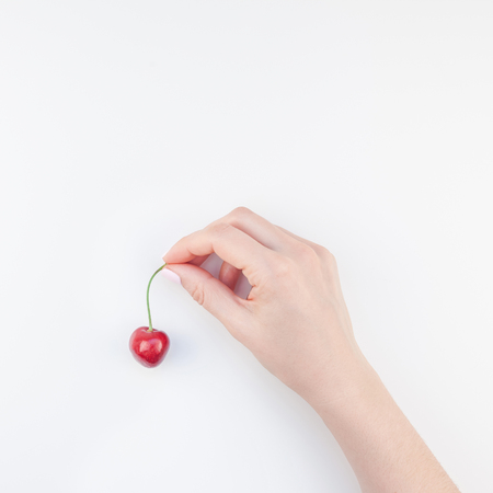 Square top view of fresh ripe cherry in a female hands with copy space isolated on white background in minimal style. Concept of summer fun and healthy eating. Template for your text or food designの写真素材