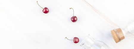 Long wide banner of glass bottles and ripe cherries with copy space isolated on marble background in...
