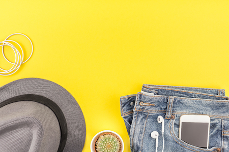 Flat lay of blue jeans, grey hat, cactus and smartphone headphones on bold yellow paper background with copy space. Overhead view of woman casual outfit. Trendy hipster look top viewの写真素材